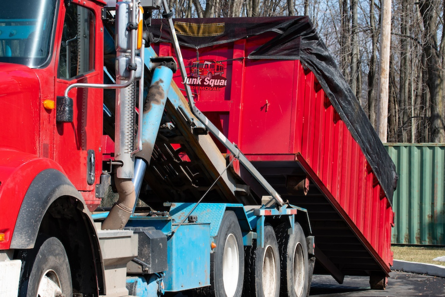 Red Junk Squad roll-off dumpster truck picking up a large container in Fort Lauderdale, equipped for efficient waste removal